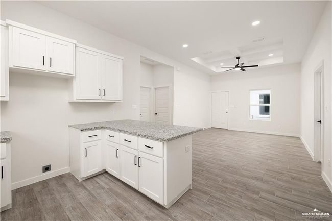 Kitchen featuring ceiling fan, a tray ceiling, a peninsula, light wood-type flooring, and white cabinetry | Image 11