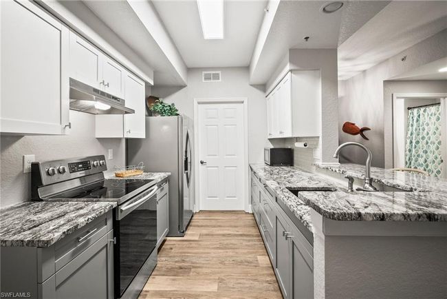 Kitchen with white cabinetry, stainless steel electric range, under cabinet range hood, light wood finished floors, and a peninsula | Image 9