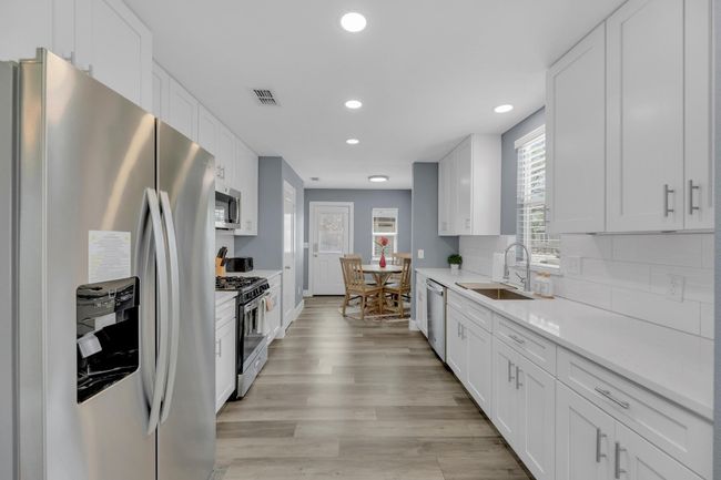 Kitchen featuring light countertops, white cabinets, stainless steel appliances, a sink, and light wood-type flooring | Image 12