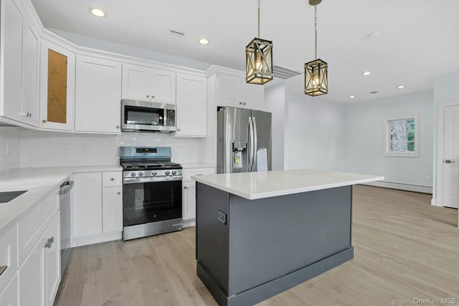 Kitchen featuring stainless steel appliances, light wood-style floors, decorative backsplash, light countertops, and white cabinets | Image 10