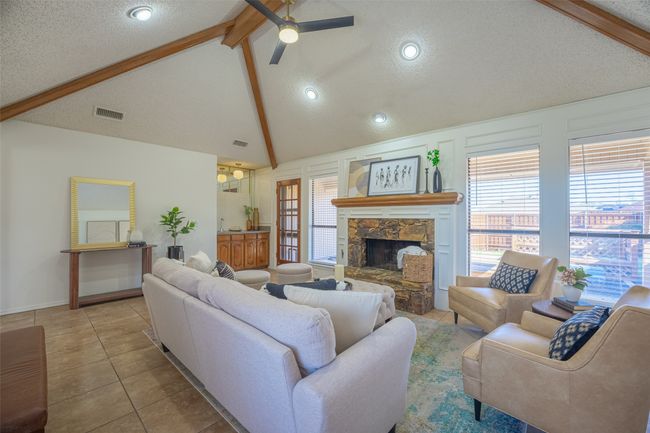 Tiled living room featuring a stone fireplace, wet bar, ceiling fan, vaulted ceiling with beams and a view of the back patio and yard | Image 6