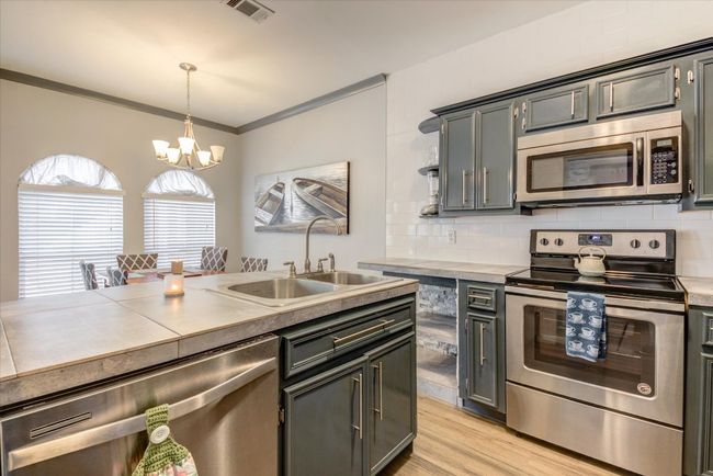 Kitchen featuring stainless steel appliances, a chandelier, hanging light fixtures, light wood-style floors, and backsplash | Image 4