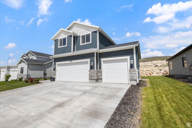 View of front facade featuring stone siding, a front lawn, concrete driveway, and an attached garage | Image 4