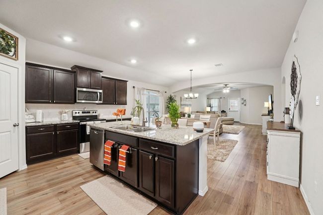Kitchen with stainless steel appliances, open floor plan, ceiling fan, dark brown cabinetry, and light wood-style flooring | Image 24