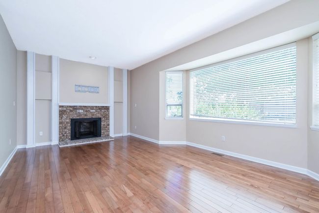 Unfurnished living room featuring baseboards, visible vents, a brick fireplace, and wood-type flooring | Image 5