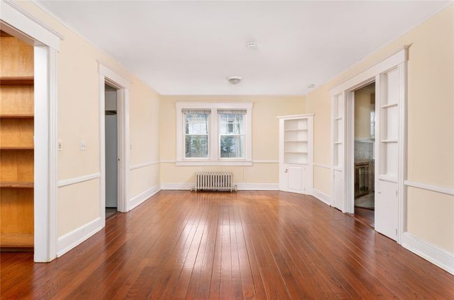 Spare room with dark wood-type flooring, radiator heating unit, a fireplace, and baseboards | Image 5