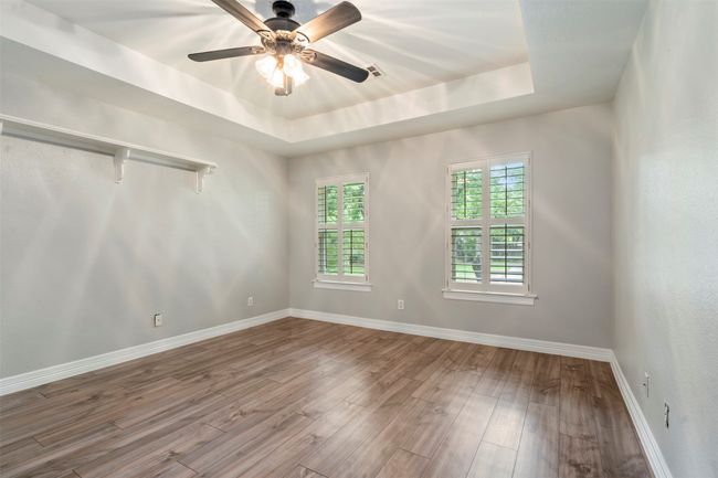 Empty room with a tray ceiling, wood finished floors, ceiling fan, and baseboards | Image 25