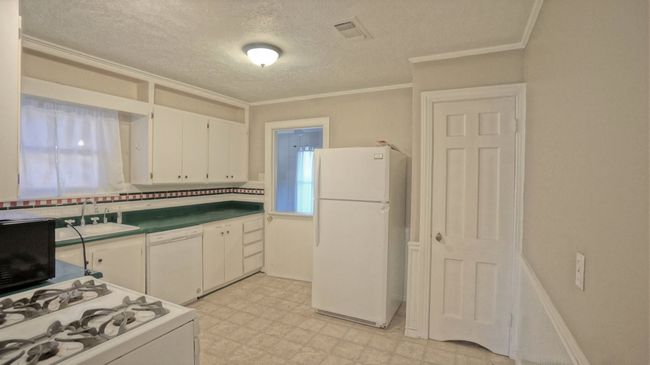 Kitchen with white appliances, light flooring, white cabinets, ornamental molding, and a textured ceiling | Image 5
