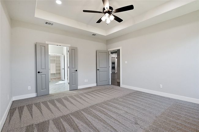 Unfurnished bedroom featuring carpet, a raised ceiling, baseboards, a spacious closet, and a ceiling fan | Image 16