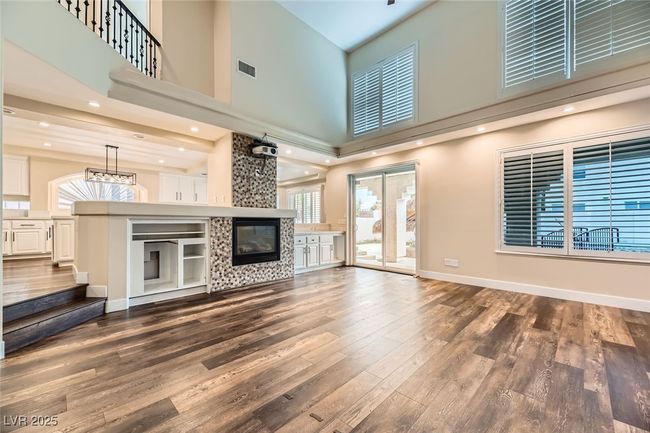 Unfurnished living room with a high ceiling, plenty of natural light, dark wood-style flooring, a fireplace, and stairs | Image 6
