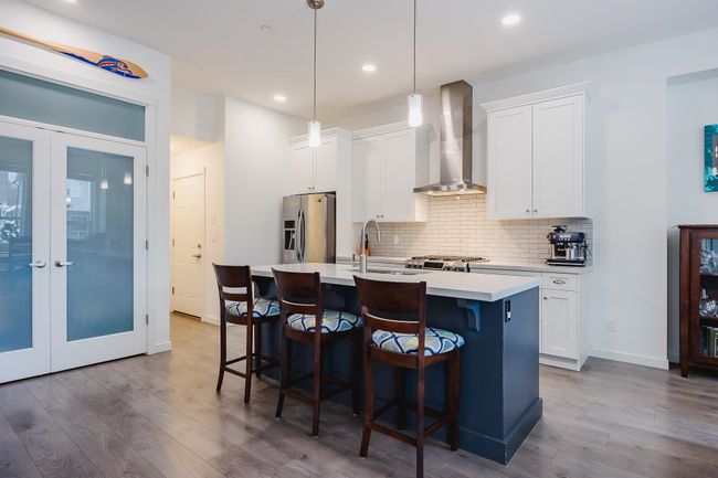 Kitchen featuring stainless steel fridge, wood finished floors, wall chimney range hood, and a center island with sink | Image 9