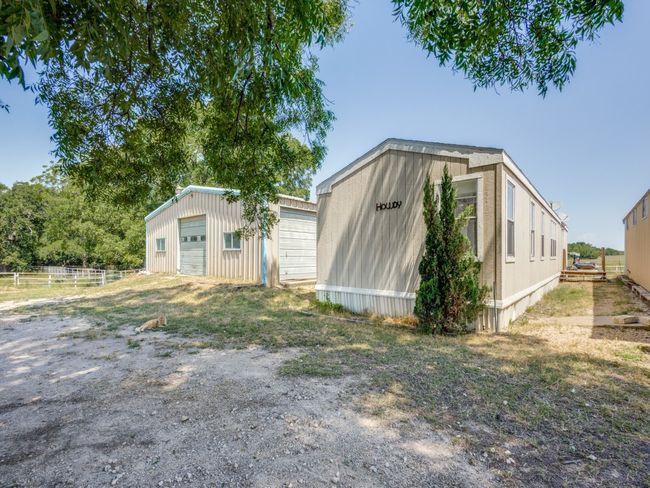 The mobile is in between the two barns. This would be the perfect space for a ranch hand, older parents, adult child getting back on his or her feet, a guest or just extra storage. The barns have windows and multiple overhead doors. Animal pens are to the left of the far barn. | Image 32