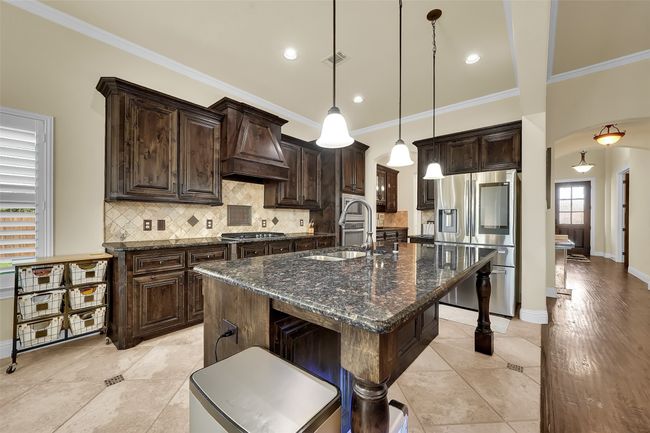 Kitchen with dark brown cabinetry, dark stone counters, backsplash, a kitchen island with sink, and crown molding | Image 4