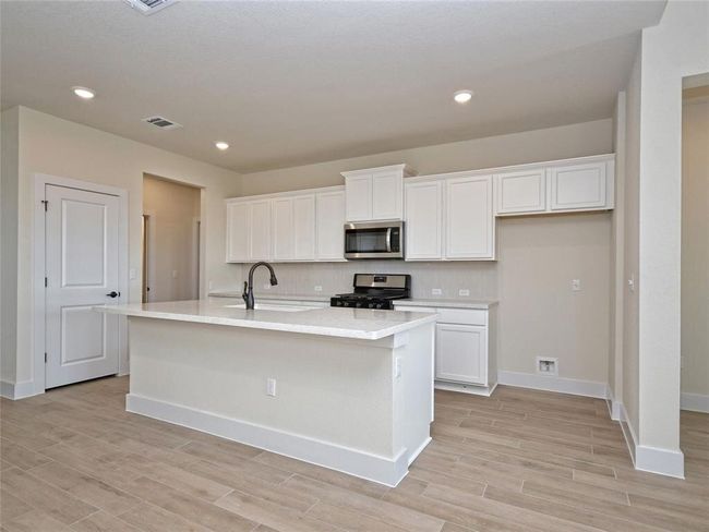 Kitchen featuring stainless steel appliances, white cabinets, light wood-style floors, an island with sink, and recessed lighting | Image 7