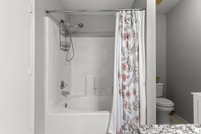Full bathroom with a textured ceiling, vanity, shower / bathtub combination with curtain, toilet, and tile patterned flooring | Image 20
