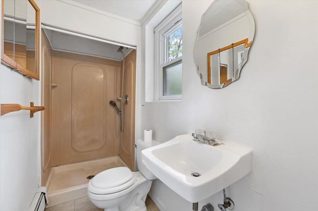 Bathroom featuring a baseboard heating unit, a shower stall, toilet, and a sink | Image 11