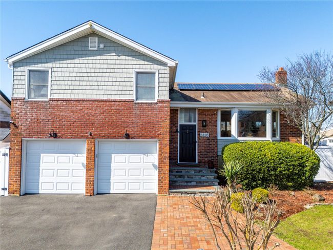 Tri-level home featuring aphalt driveway, a chimney, an attached garage, solar panels, and brick siding | Image 43