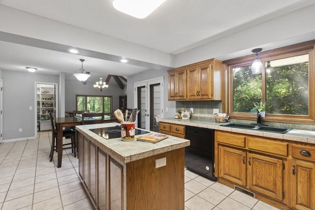 Chef’s kitchen featuring custom cabinetry, center island with cooktop, double ovens, ceramic tile floors, counters, and backsplash. Enjoy new/newer stainless steel appliances, a large window, and a fully enclosed walk-in pantry. | Image 10