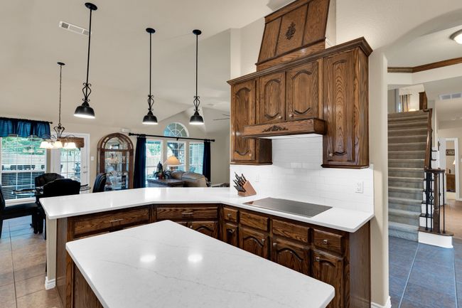 Kitchen with black electric cooktop, a peninsula, light countertops, tile patterned flooring, and decorative backsplash | Image 11