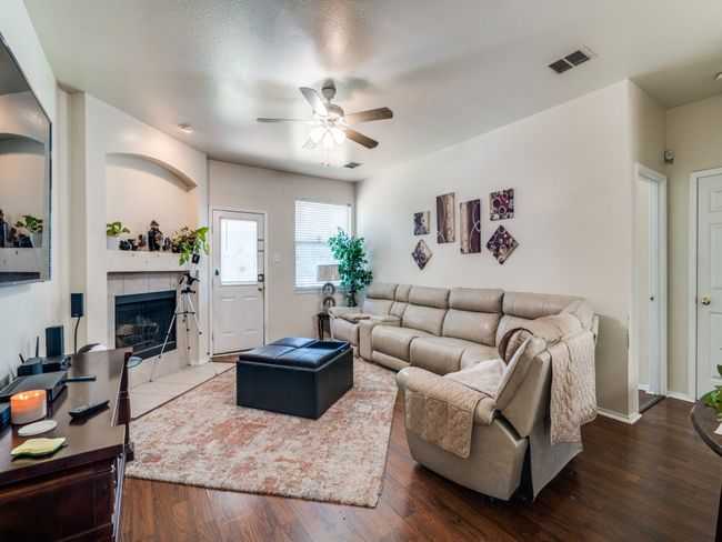 Living room with wood finished floors, visible vents, a ceiling fan, baseboards, and a tiled fireplace | Image 6