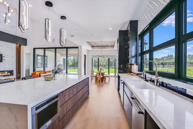 Kitchen with modern cabinets, wall of windows, dishwasher, plenty of natural light, and light wood flooring, island with microwave built in | Image 16