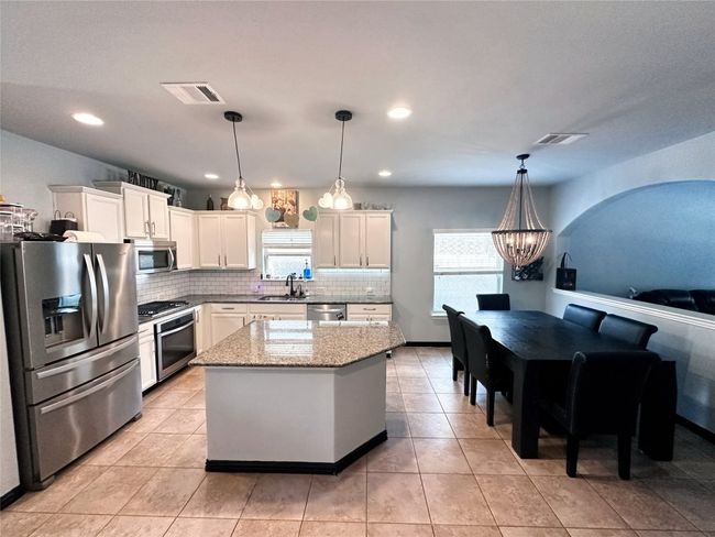 Kitchen featuring appliances with stainless steel finishes, decorative backsplash, a chandelier, white cabinetry, and light stone counters | Image 8