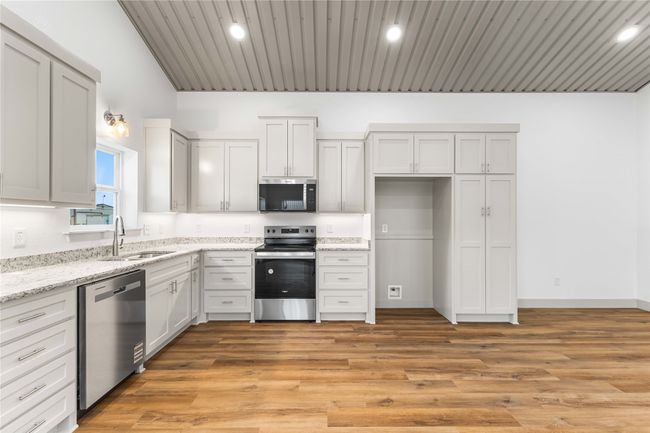 Kitchen with stainless steel appliances, a sink, light stone counters, lofted ceiling, and light wood-style floors | Image 15