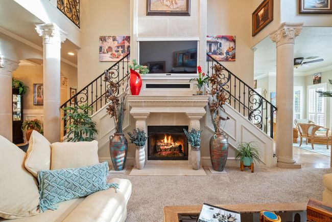 Living room featuring decorative columns, a tile fireplace, ornamental molding, stairs, and a towering ceiling | Image 19