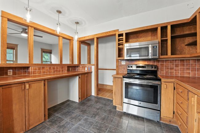 Ample counter space with custom tile work, pendant lighting, and open shelving—perfect for meal prep or as a breakfast bar. | Image 14
