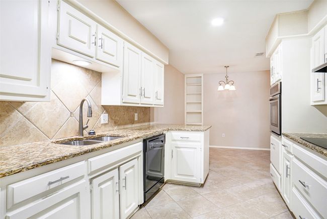 Kitchen with a sink, black dishwasher, backsplash, white cabinetry, and a peninsula | Image 4