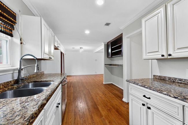 Kitchen with wood finished floors, crown molding, white cabinets, dark stone counters, and recessed lighting | Image 9