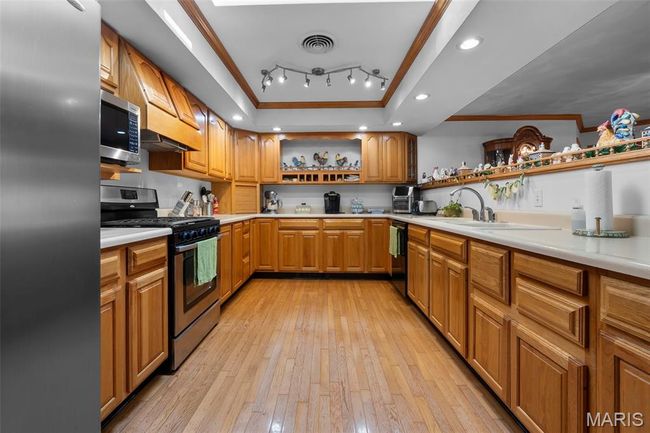 Kitchen featuring open shelves, appliances with stainless steel finishes, ornamental molding, light wood finished floors, and light countertops | Image 67