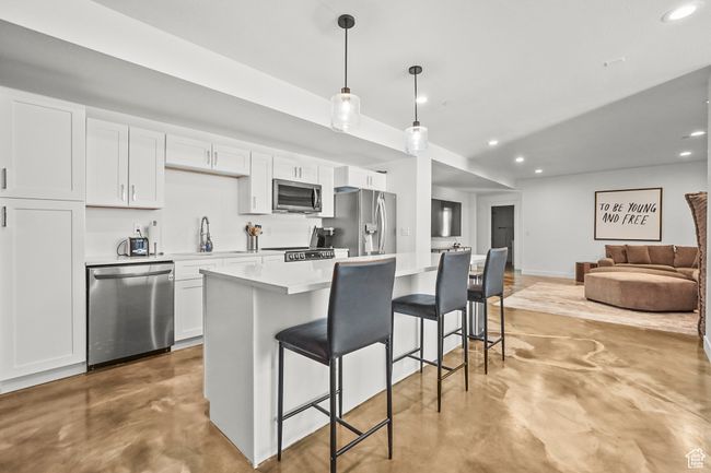 Kitchen with appliances with stainless steel finishes, finished concrete flooring, a breakfast bar area, recessed lighting, and white cabinets | Image 27