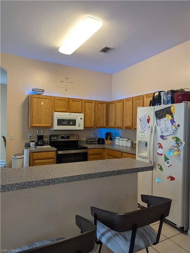 Kitchen featuring white appliances, light tile patterned flooring, a kitchen bar, and brown cabinets | Image 20
