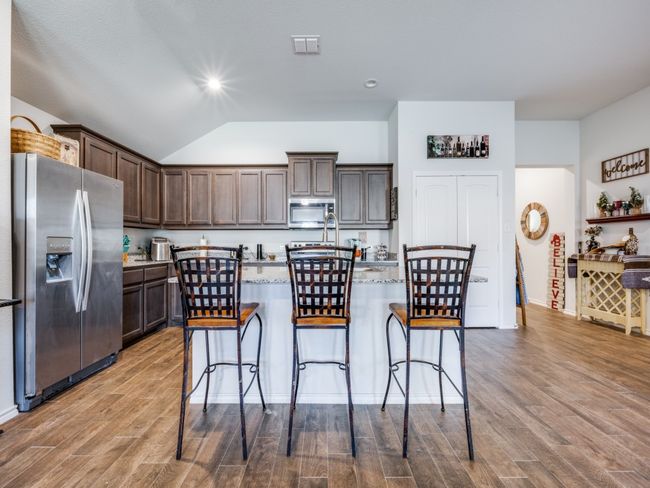 Kitchen featuring stainless steel appliances, dark brown cabinetry, wood finished floors, lofted ceiling, and a kitchen bar | Image 10