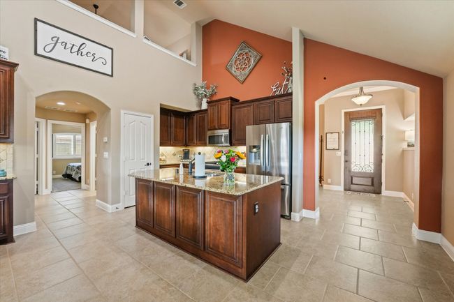 Kitchen with light stone counters, an island with sink, arched walkways, stainless steel appliances, and backsplash | Image 9