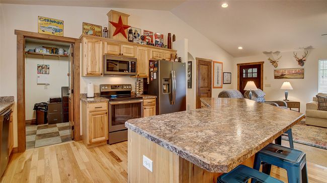 Kitchen featuring appliances with stainless steel finishes, lofted ceiling, a kitchen bar, open floor plan, and light wood-style floors | Image 10