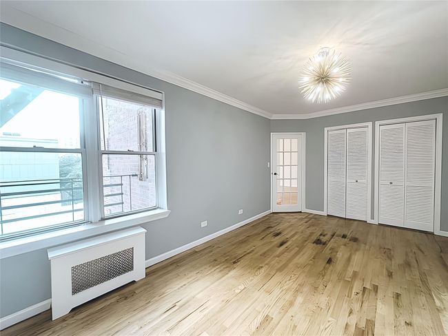 Unfurnished bedroom featuring radiator heating unit, crown molding, a chandelier, light wood-type flooring, and multiple closets | Image 9