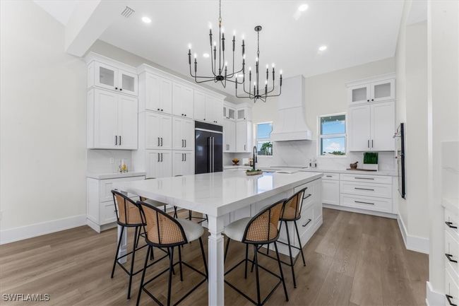 Kitchen with high end black refrigerator, a chandelier, a breakfast bar area, a large island, and wood finished floors | Image 5