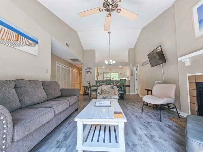 Living area with a chandelier, wood finished floors, high vaulted ceiling, a ceiling fan, and a tile fireplace | Image 7