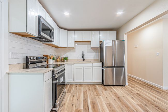 Kitchen featuring stainless steel appliances, a sink, baseboards, white cabinetry, and light countertops | Image 10