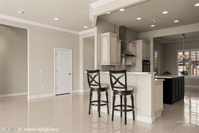 Kitchen featuring a kitchen breakfast bar, black oven, wall chimney range hood, a peninsula, and visible vents | Image 22