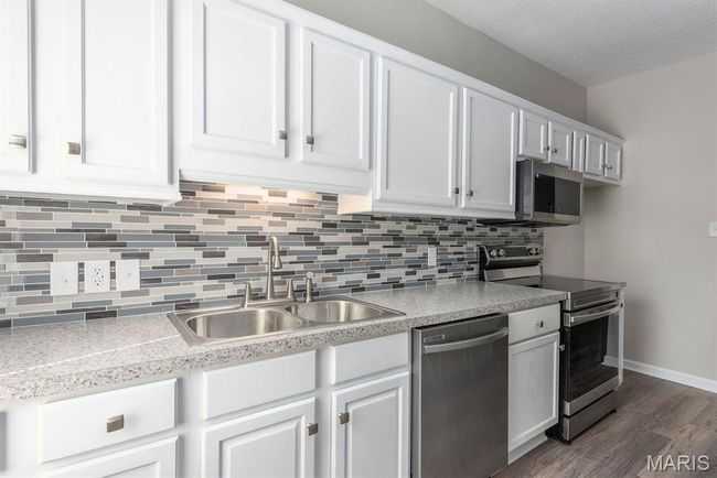 Kitchen with stainless steel appliances, dark wood-style flooring, decorative backsplash, and white cabinets | Image 9