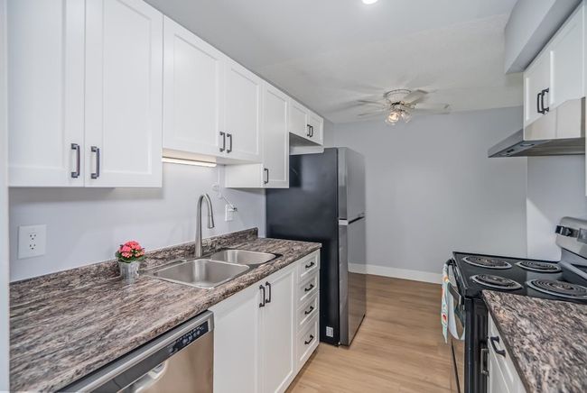 Kitchen featuring stainless steel appliances, a sink, under cabinet range hood, ceiling fan, and baseboards | Image 6