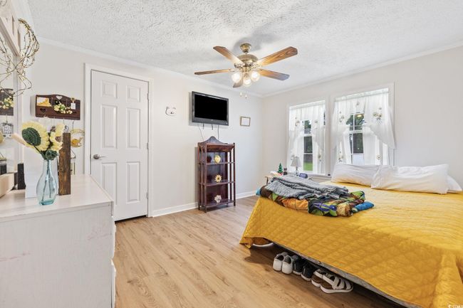 Bedroom featuring wood finished floors, a ceiling fan, a textured ceiling, and crown molding | Image 18