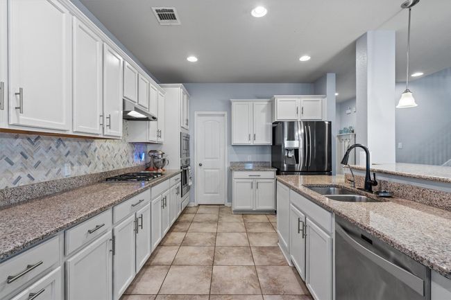 Kitchen featuring stainless steel appliances, a sink, white cabinetry, under cabinet range hood, and light stone counters | Image 14