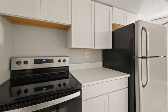 Kitchen featuring stainless steel electric range, freestanding refrigerator, light countertops, white cabinetry, and a textured ceiling | Image 6