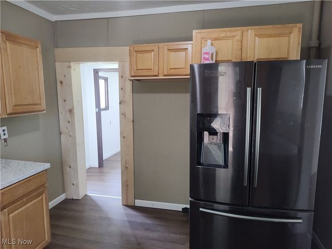 Kitchen featuring fridge with ice dispenser, light brown cabinetry, dark wood-type flooring, light stone counters, and baseboards | Image 23