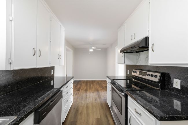 Kitchen featuring stainless steel appliances, under cabinet range hood, dark wood finished floors, ceiling fan, and white cabinetry | Image 18