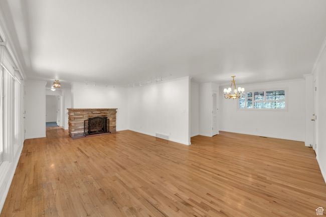Unfurnished living room with a chandelier, a stone fireplace, light wood finished floors, and baseboards | Image 13